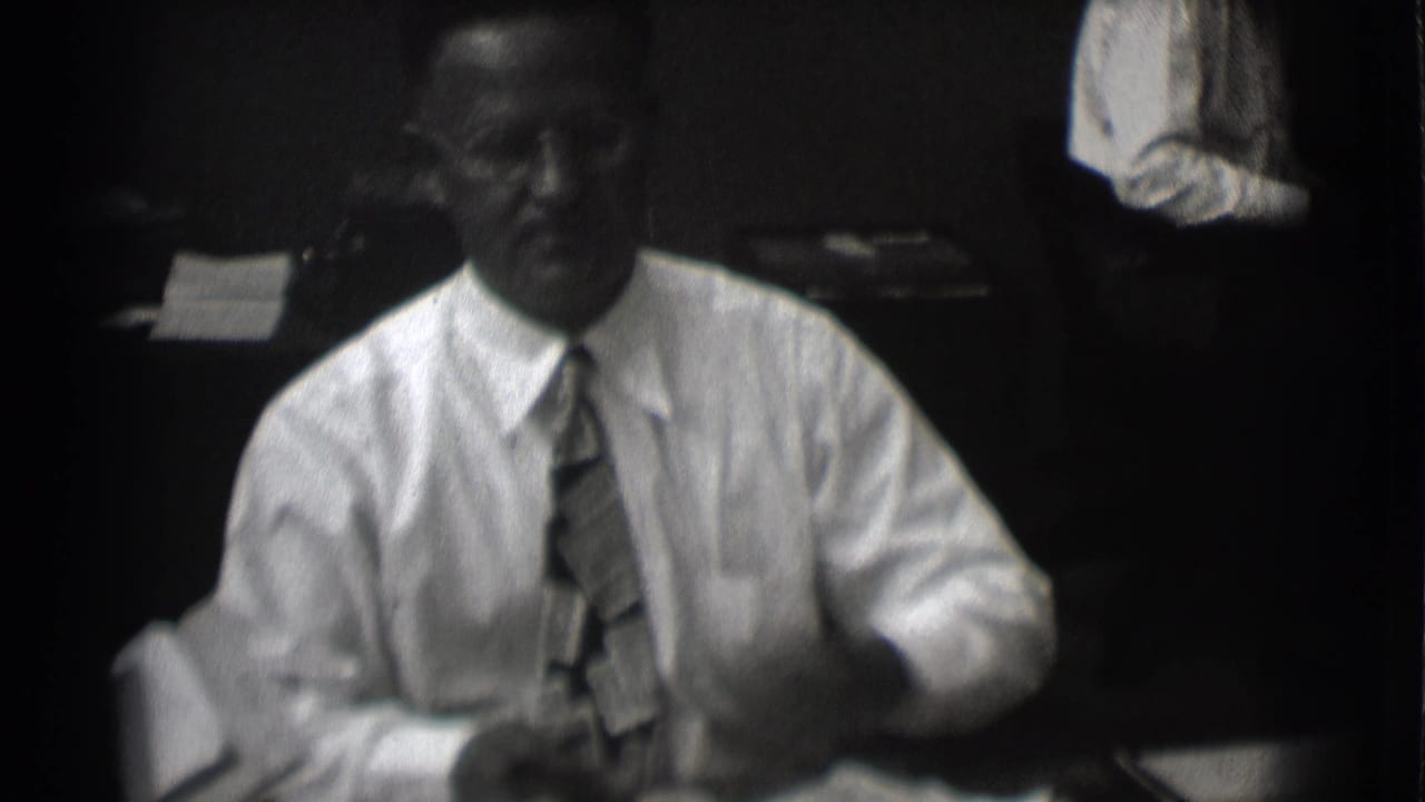 Man in white shirt and tie seated at an office desk.