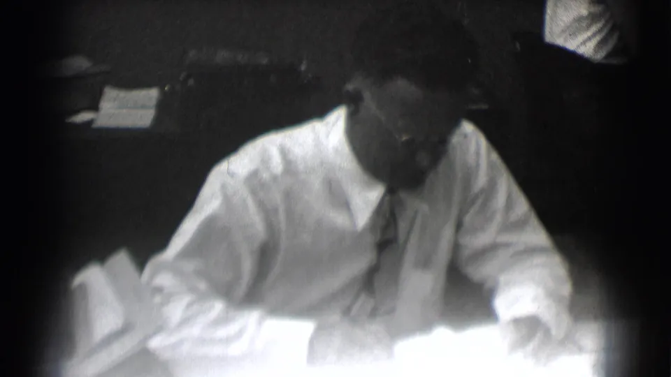 The Saint Louis office worker studies or writes on bright desk papers as the frame overexposes near the bottom edge.