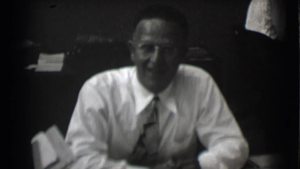 In 1959 Saint Louis footage, a man in glasses, white shirt, and tie sits at a desk in a dim office interior.