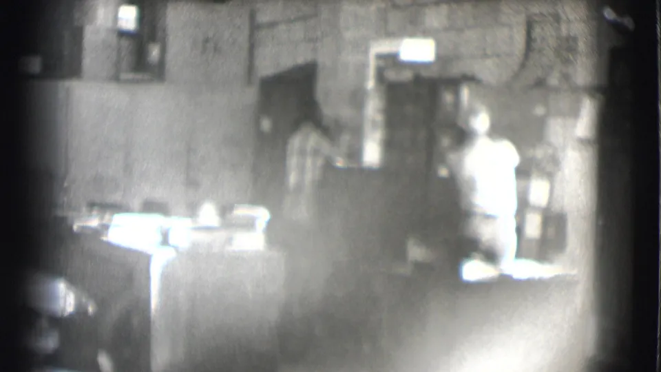 A 1959 Saint Louis office view shows a seated man at a desk with another person visible near shelves or a cabinet.