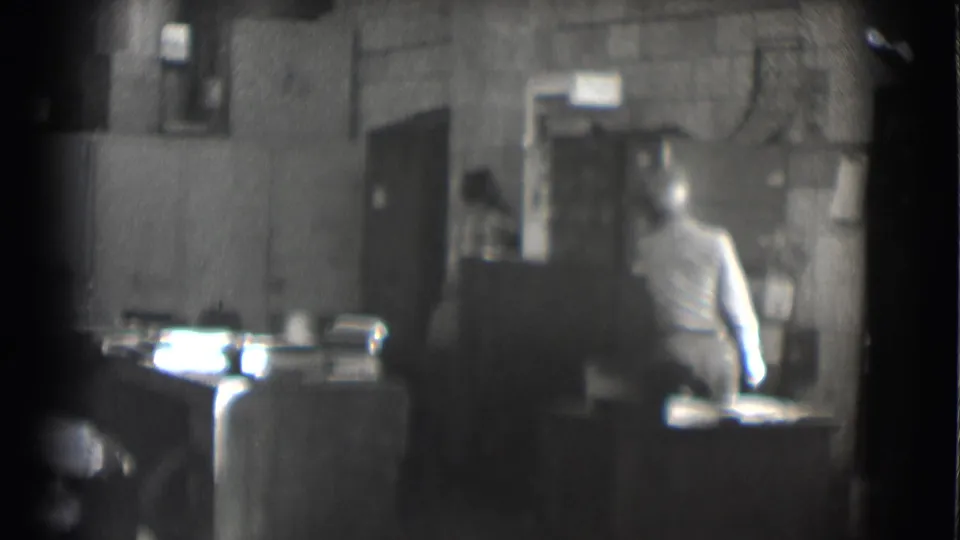 The suited man gestures from his desk in the Saint Louis office, with another person still visible near the back wall.