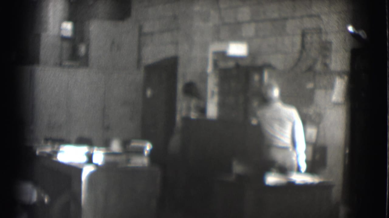 1959 Saint Louis office interior with a seated man at a desk, soft focus and visible black-and-white film grain.
