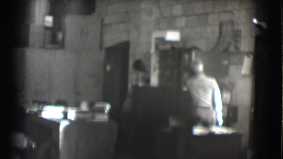 1959 Saint Louis office interior with a seated man at a desk, soft focus and visible black-and-white film grain.