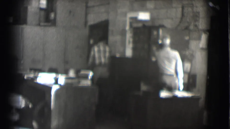 1959 Saint Louis 8mm frame with a plaid-shirted person near a doorway behind a man seated at a desk.
