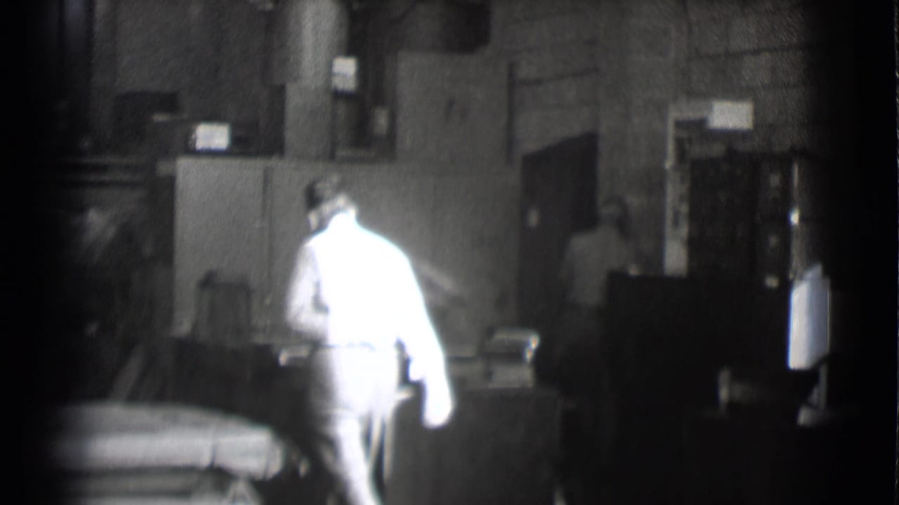 Man in a bright shirt walking through a dim office with desks and equipment.