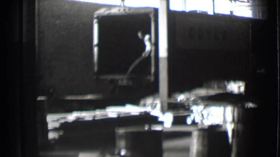Black-and-white 8mm view of a Saint Louis industrial loading area with sheet metal, a truck side, and bright window glare.