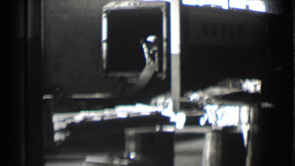 A worker is visible in the 1959 factory loading area, positioned near sheet metal and a truck marked with partial lettering.