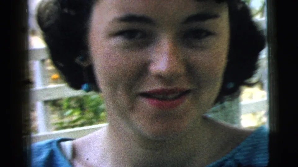 The 1961 Camden home movie shows the woman close to the lens, smiling softly with blue earrings visible beside a white railing.