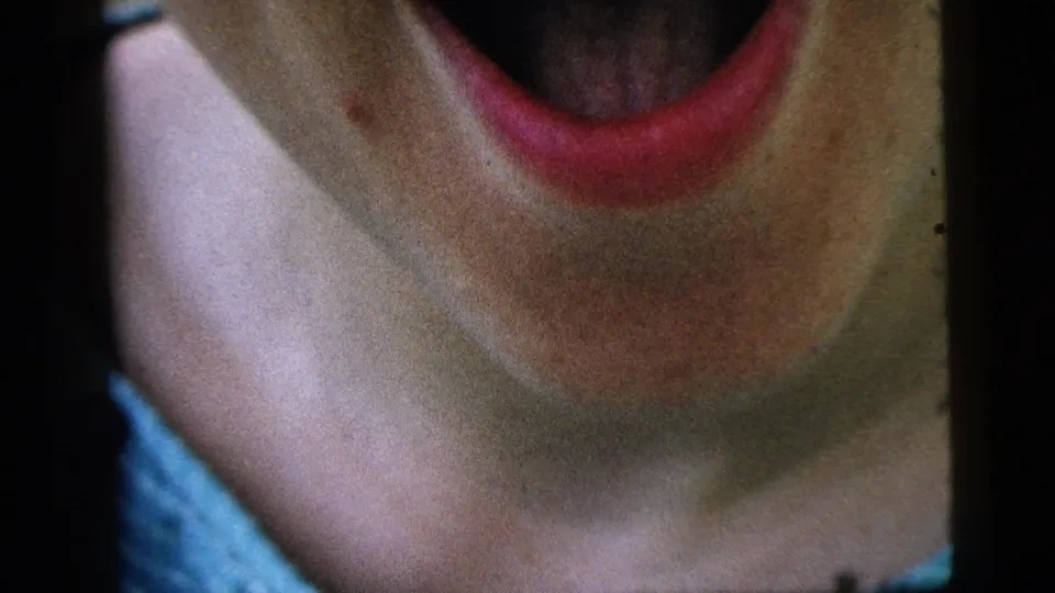 Close cropped 8mm frame from Camden in 1961 shows the woman laughing, with her mouth, neck, shoulder, and blue top filling the frame.