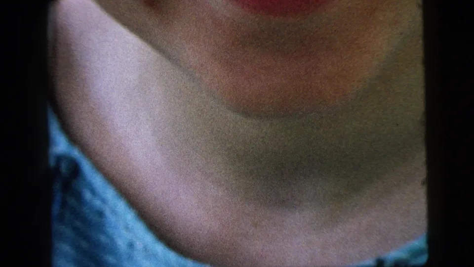 Soft 1961 8mm close-up from Camden shows the woman's lower face, neck, and blue top as the laugh settles.