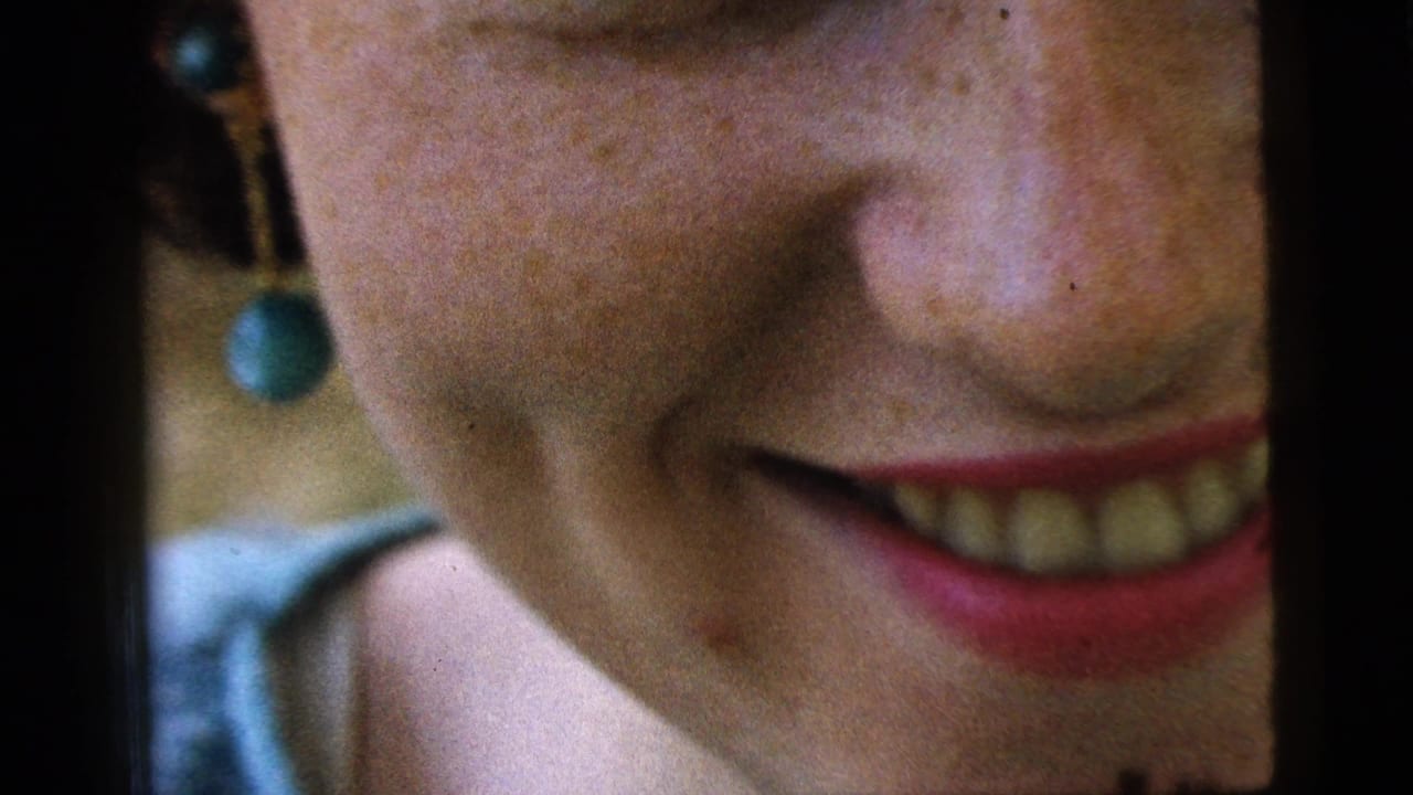 Close view of a smiling woman's cheek, nose, mouth, and dangling green earring.