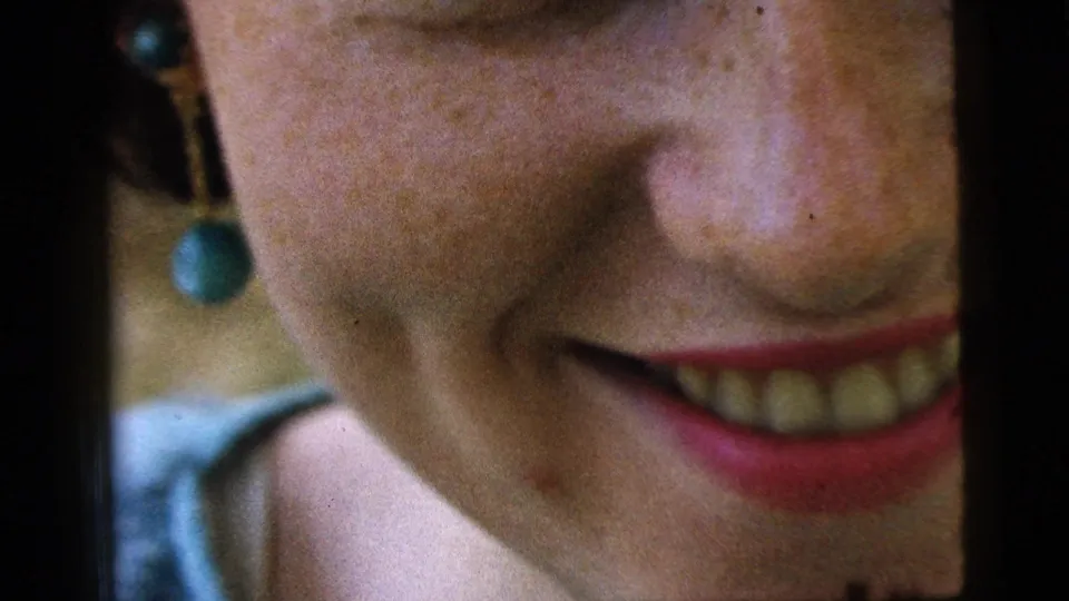 Camden 1961 8mm close-up showing the woman's partial face, smile, freckles, and dangling green earring.