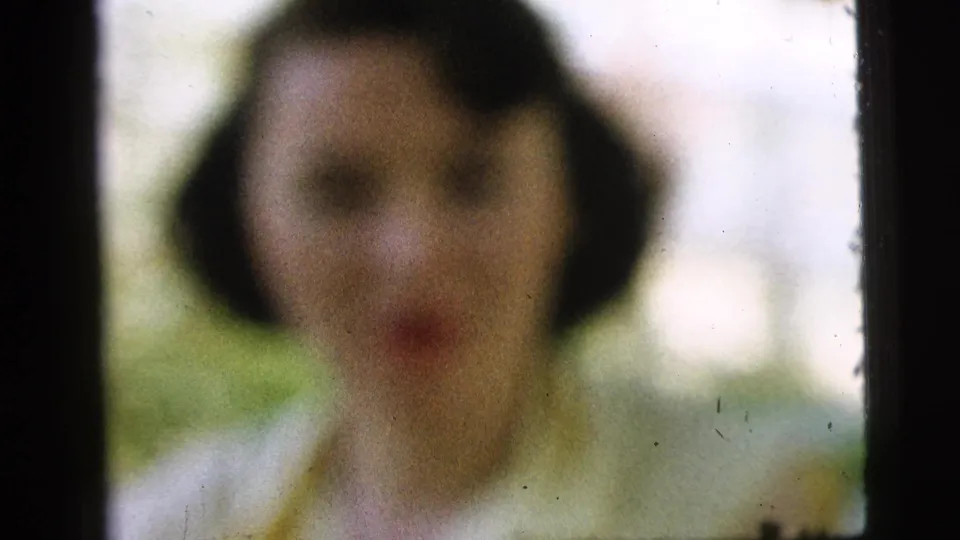 Camden 1961 8mm frame with the woman blurred at a distance, facing the camera against a bright outdoor background.