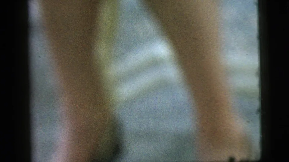 Out-of-focus Camden 1961 frame showing a figure near pale outdoor furniture, with green and white background shapes.