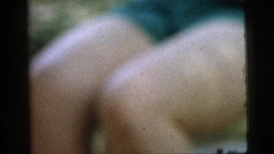 Soft-focus 1961 Camden home-movie frame showing a close, blurred view of a person's leg near dark vertical porch framing.