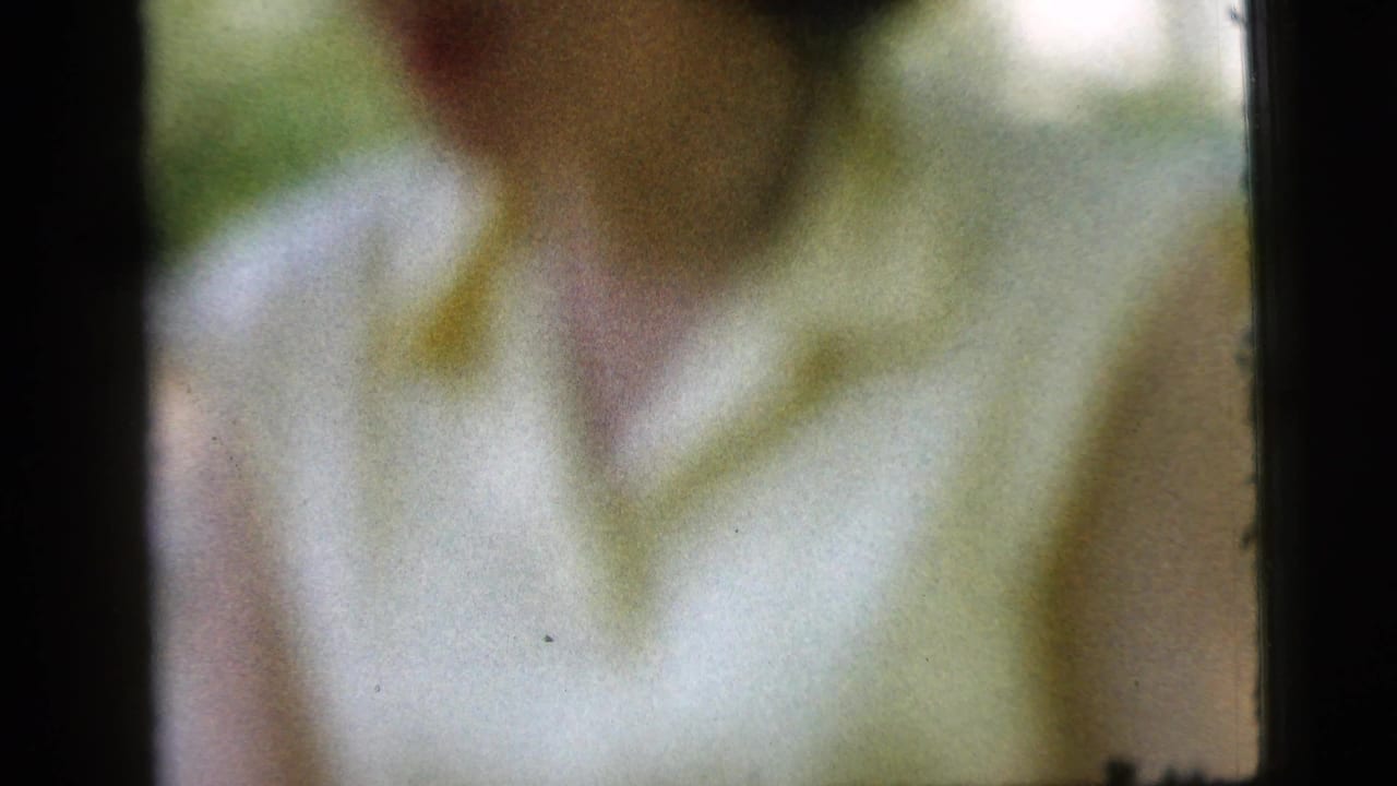 Blurred close-up of a woman in a light blouse near porch framing.