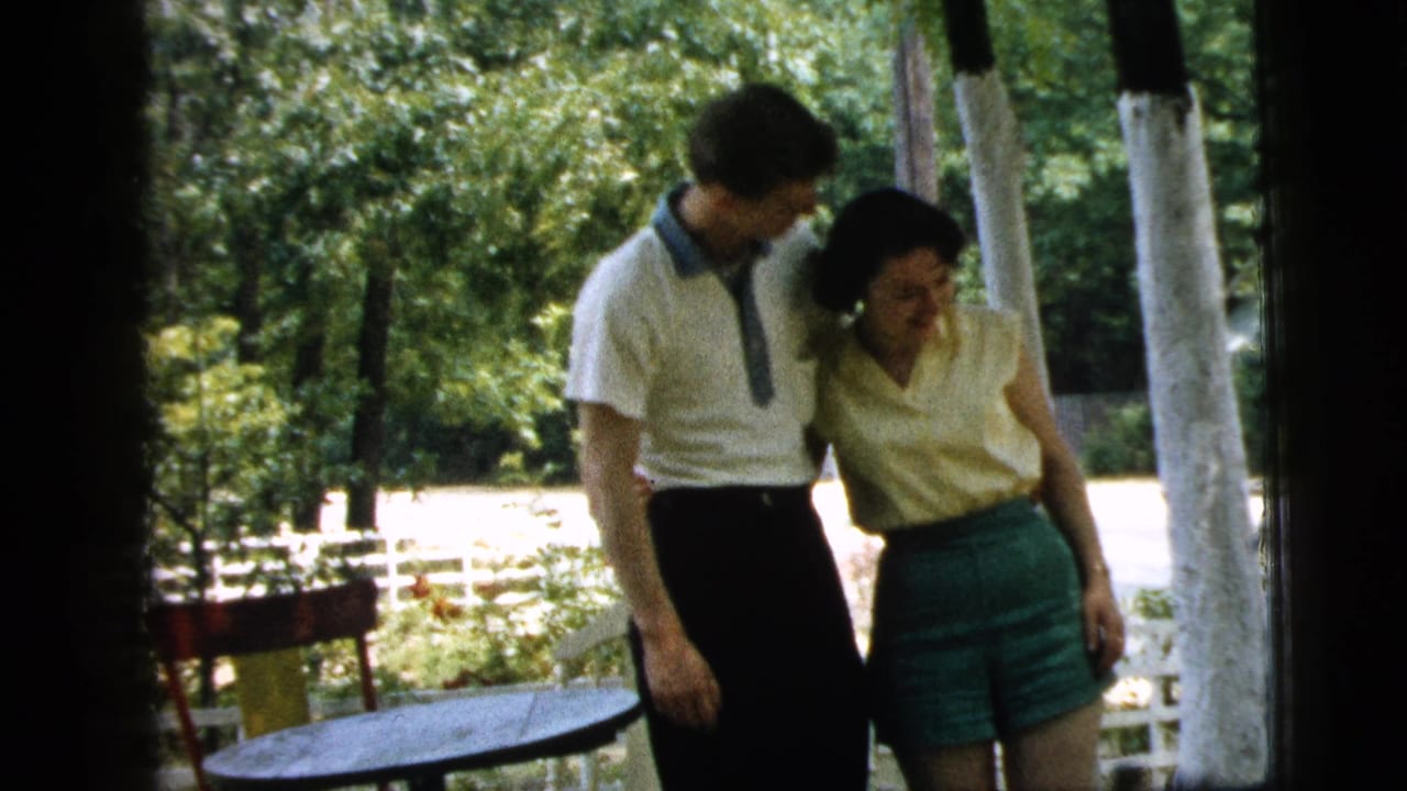The couple remains close together on the Camden porch, with the man looking down toward the woman amid bright trees and yard light.