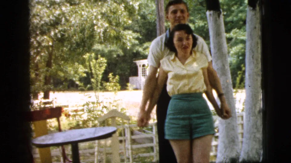 The man remains behind the woman as they move or pose together in the Camden, New Jersey outdoor scene.