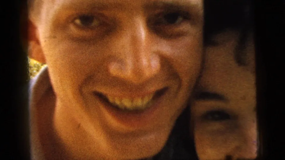 The couple leans very close to the 8mm camera, with the man smiling broadly and the woman partly visible beside him.