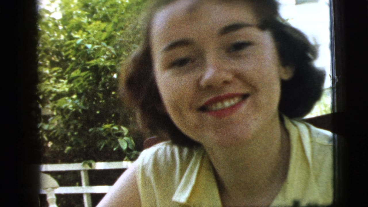 Young woman in a yellow blouse smiles close to the camera outdoors.