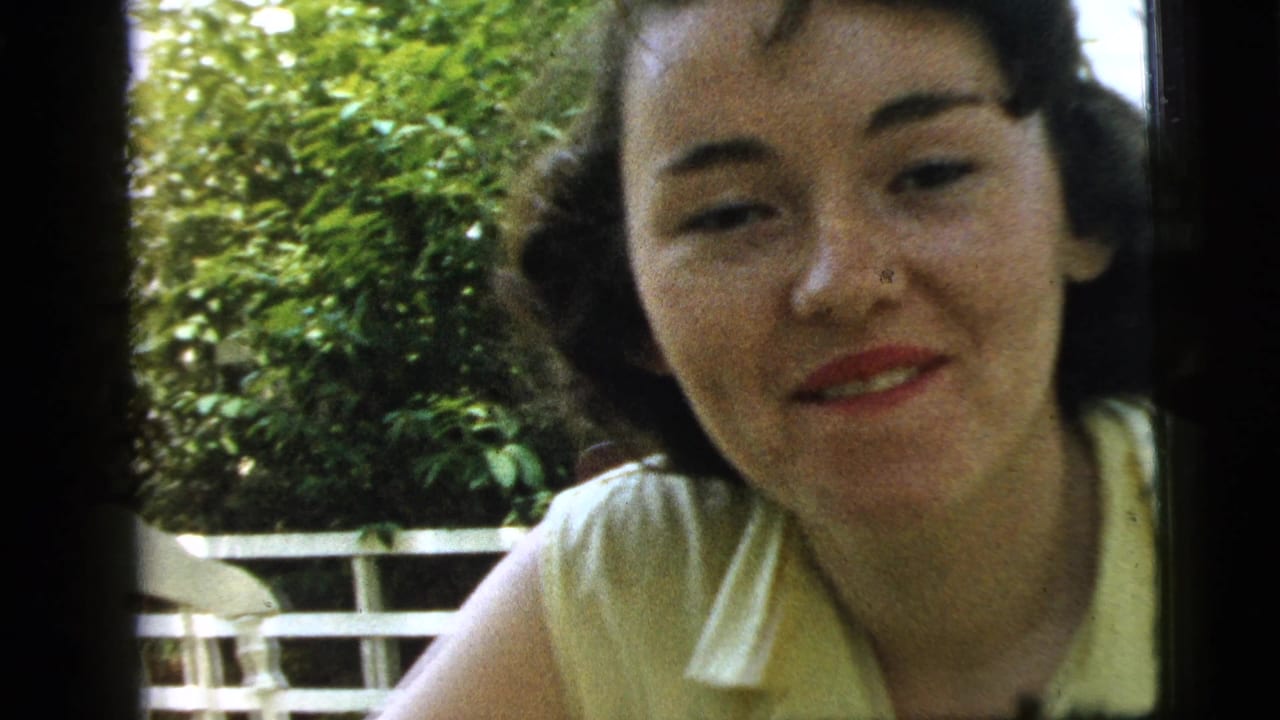 Young woman faces the camera with a soft smile near leafy greenery.