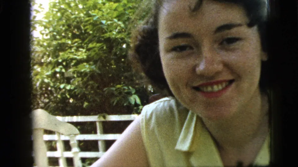 Young woman in a yellow blouse smiles with her head slightly lowered in Camden, New Jersey home-movie footage from 1961.