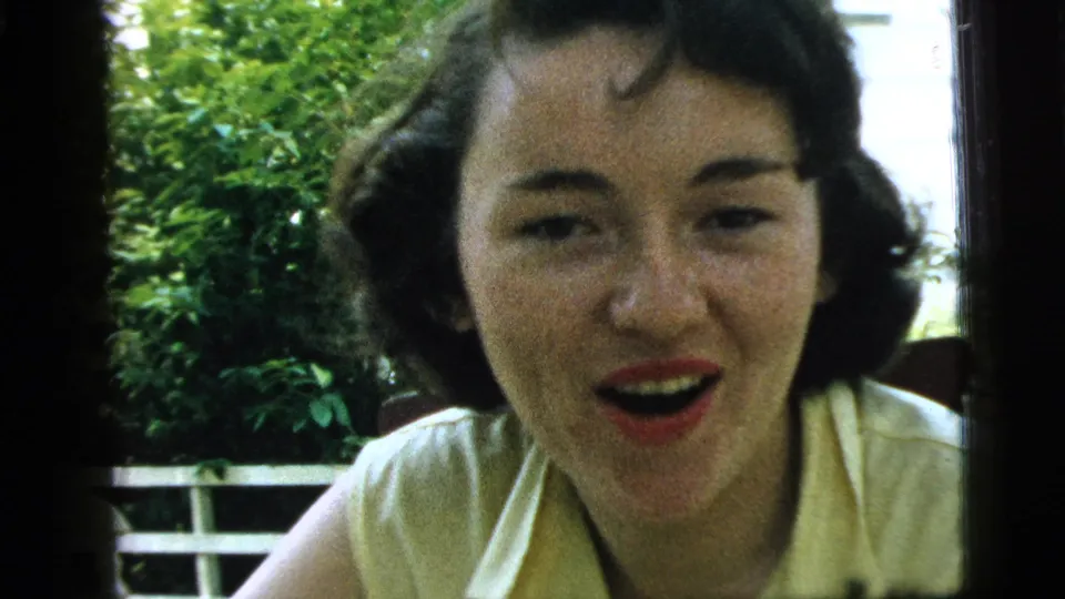 This 1961 Camden 8mm frame shows the woman facing the camera, mouth open as if talking, framed by a window and greenery.