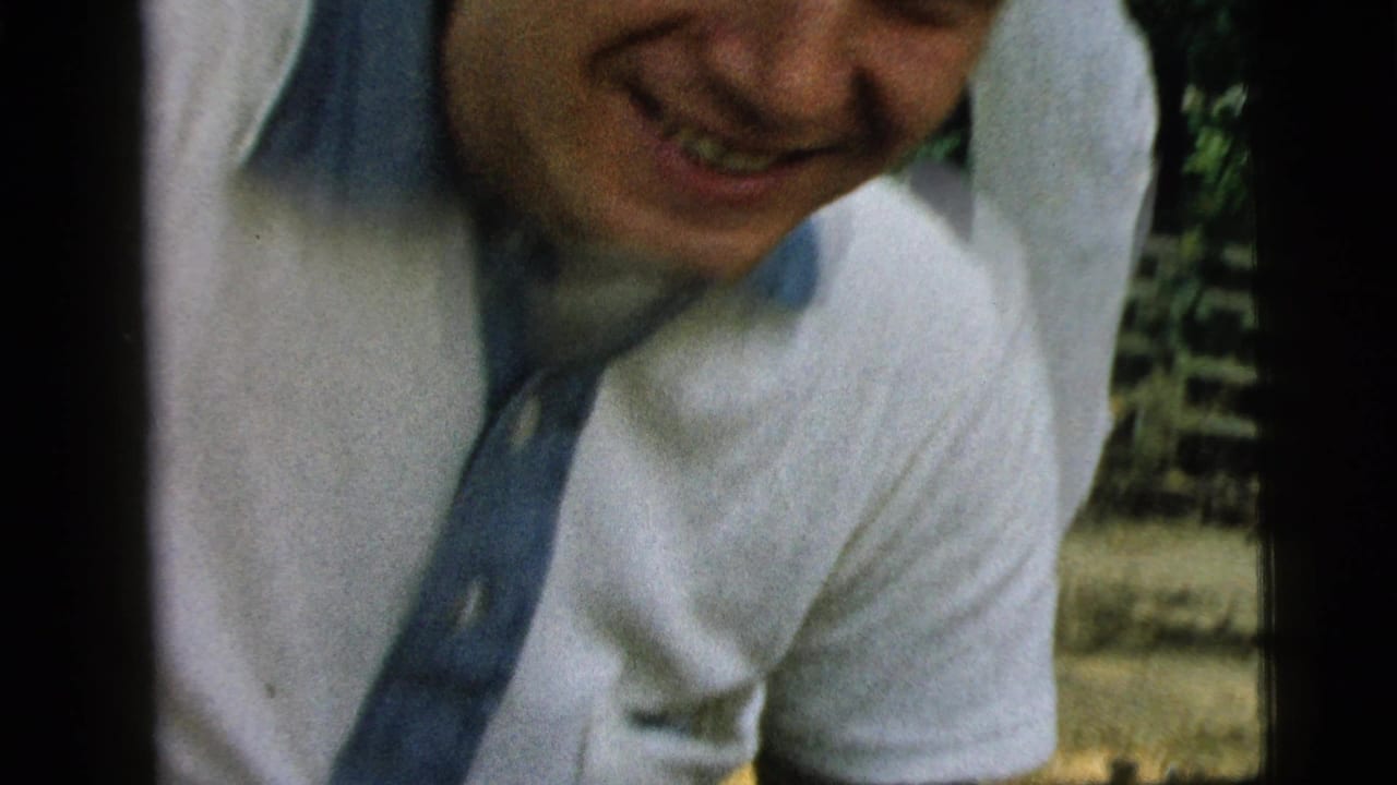In the Camden 1961 outdoor home movie, the young man smiles while leaning down, partly cropped by the close handheld framing.