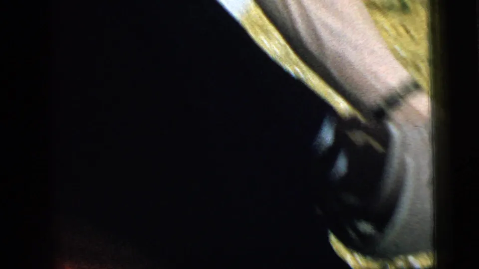 A close cropped view shows the young man's leg and dark shoe as he bends down outdoors in the Camden, New Jersey home-movie clip.