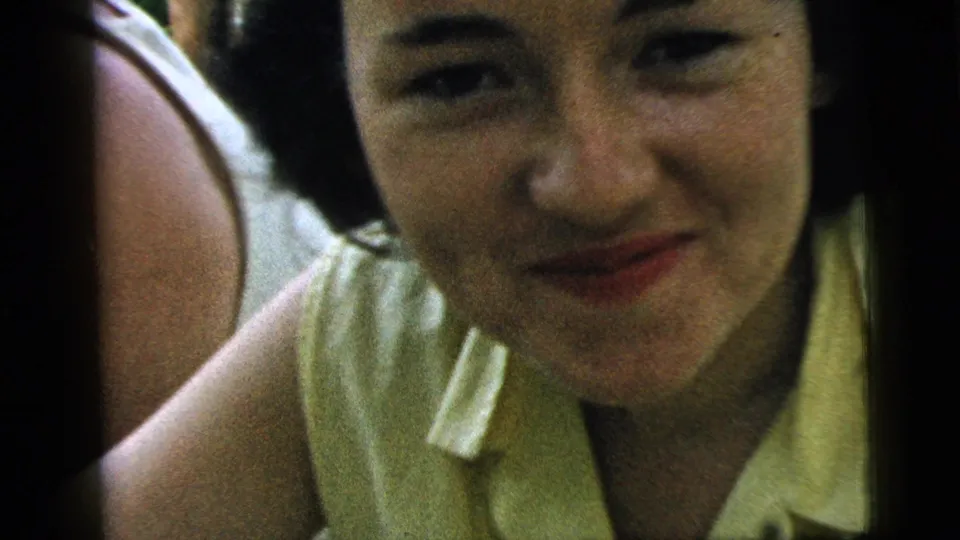 Close-up of an adult woman in a yellow sleeveless top smiling toward the camera in 1961 Camden home-movie footage.