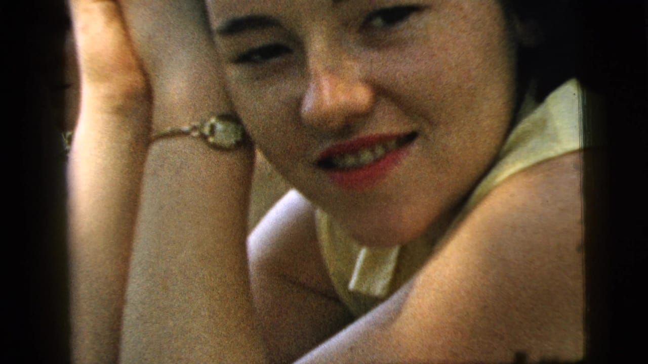 Close-up of a young woman leaning on her hand, wearing red lipstick and a pale collared top.