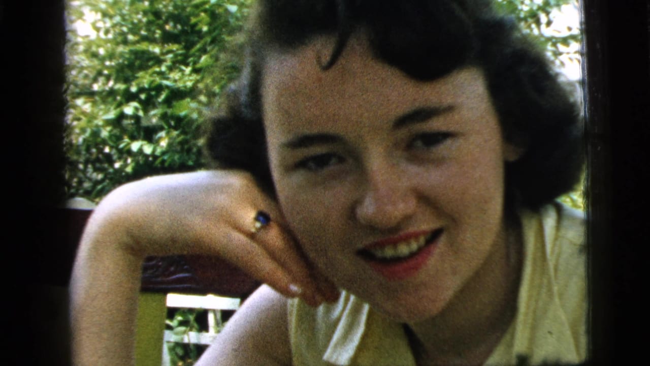 Young woman leans close to the camera, smiling with a ringed hand by her cheek.