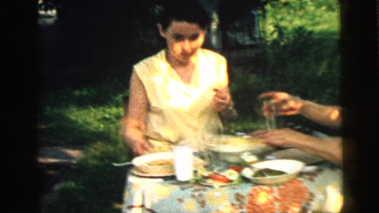Woman seated outdoors at a table with plates, bowls, and cups.