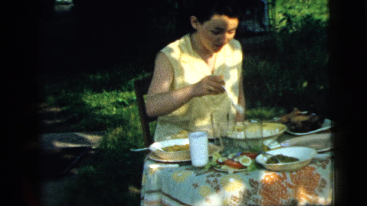 Woman in a light sleeveless dress eating at an outdoor table.