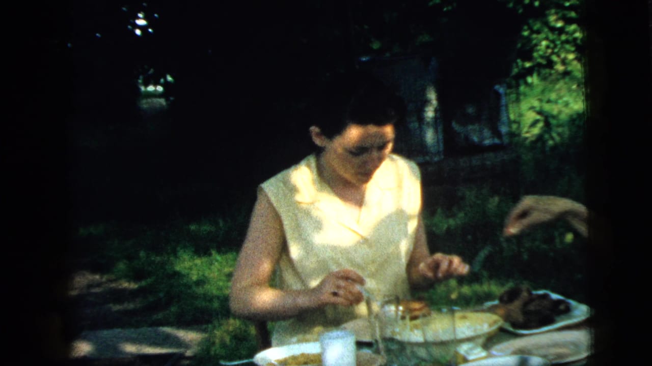 Woman seated at an outdoor table while another person's arm reaches toward the food.
