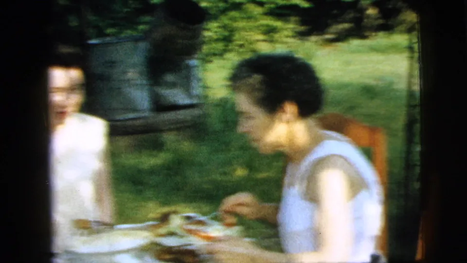 1961 Camden backyard dining frame with a woman in a white sleeveless top eating beside another seated woman.