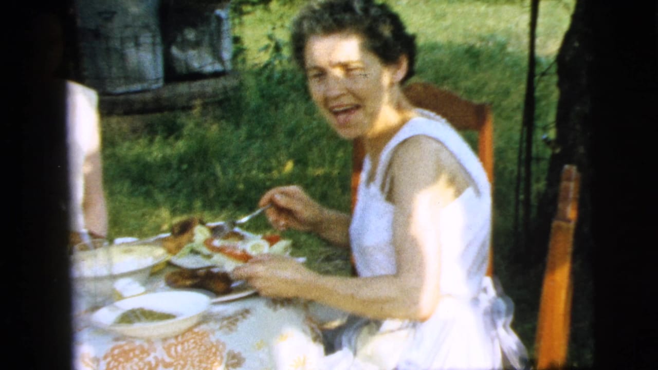 Woman in a white sleeveless dress eating at an outdoor table in a garden.