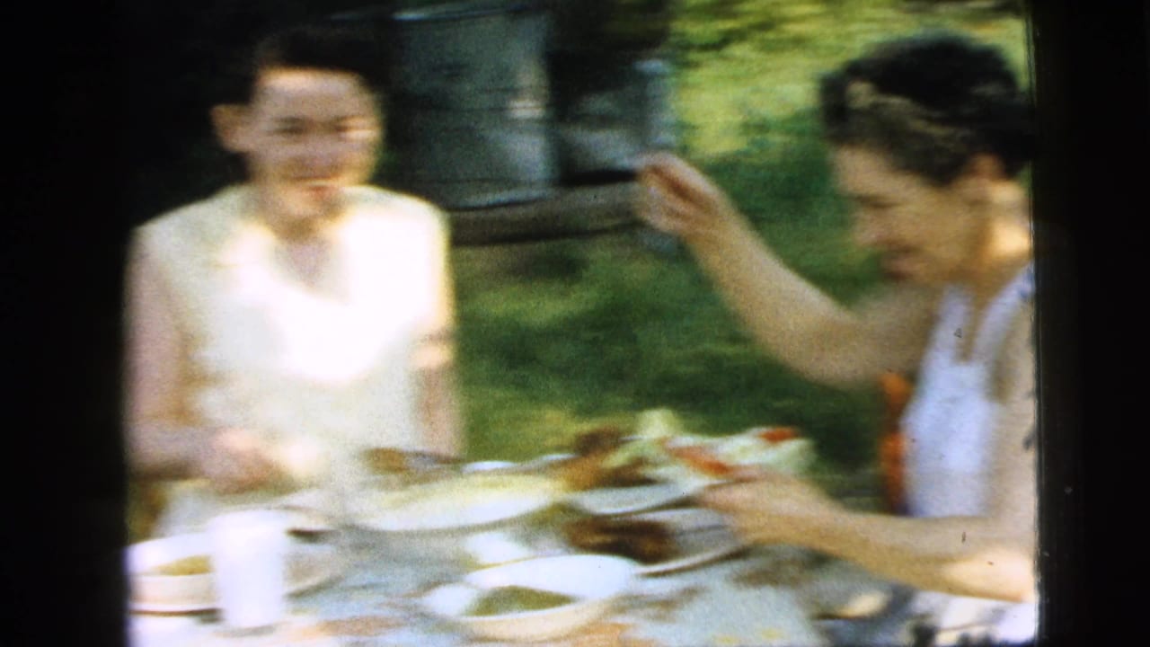 Two women sit at a sunny outdoor lunch table in Camden, New Jersey, with plates, salad, glasses, and a floral tablecloth visible in the 8mm frame.