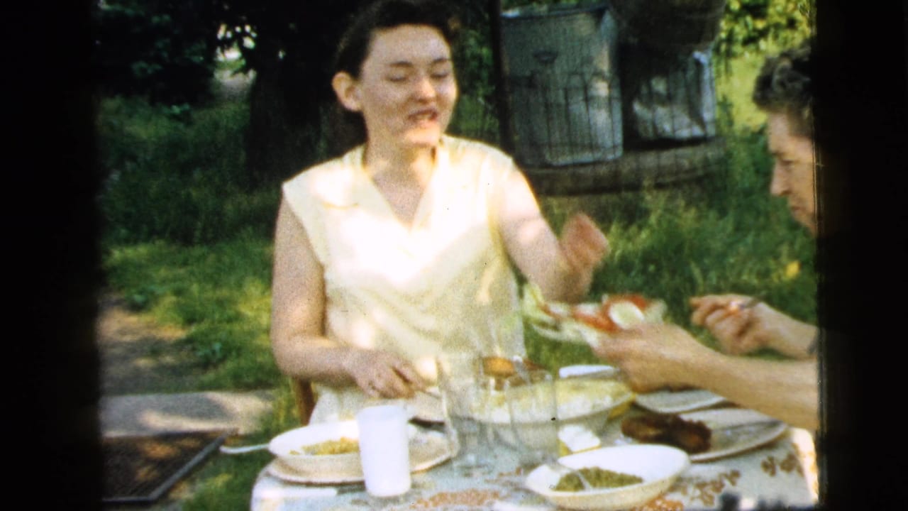 In Camden, New Jersey, 1961, two adult women share a garden meal at a table set with plates, glasses, bread, and salad.