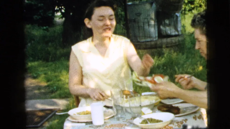 In Camden, New Jersey, 1961, two adult women share a garden meal at a table set with plates, glasses, bread, and salad.
