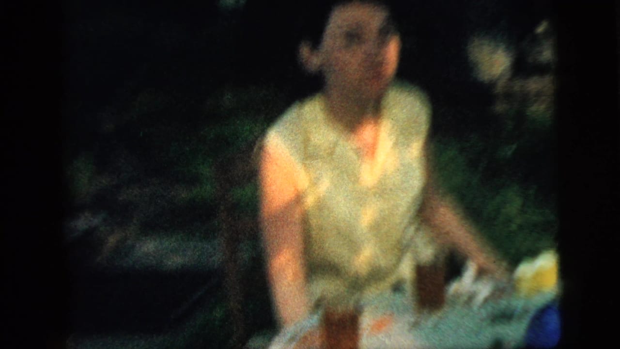 Soft-focus woman in a yellow sleeveless blouse seated outdoors at a table.