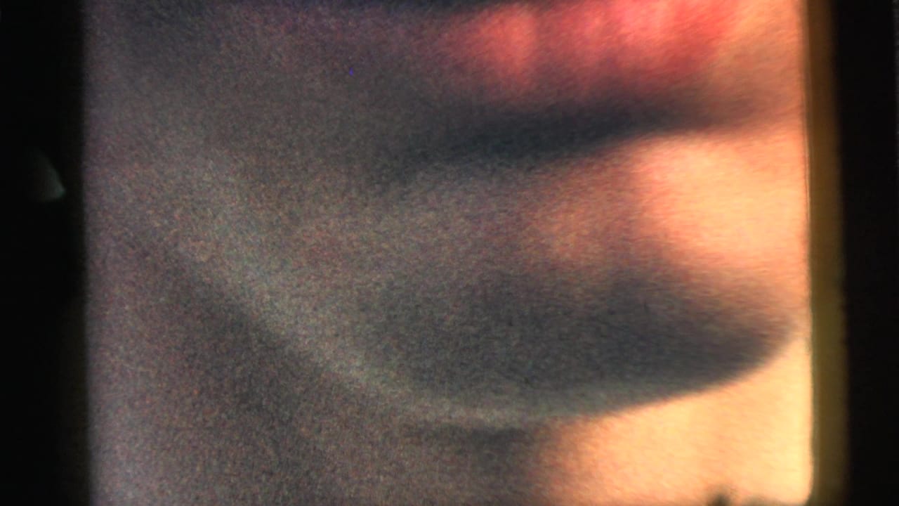 Blurred close-up film frame with warm skin tones and dark edge artifacts.