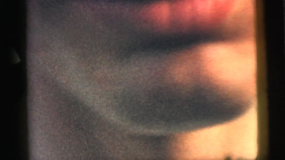 A heavily blurred 8mm frame from the 1961 Camden clip, showing indistinct warm tones and dark film borders before the backyard scene resolves.