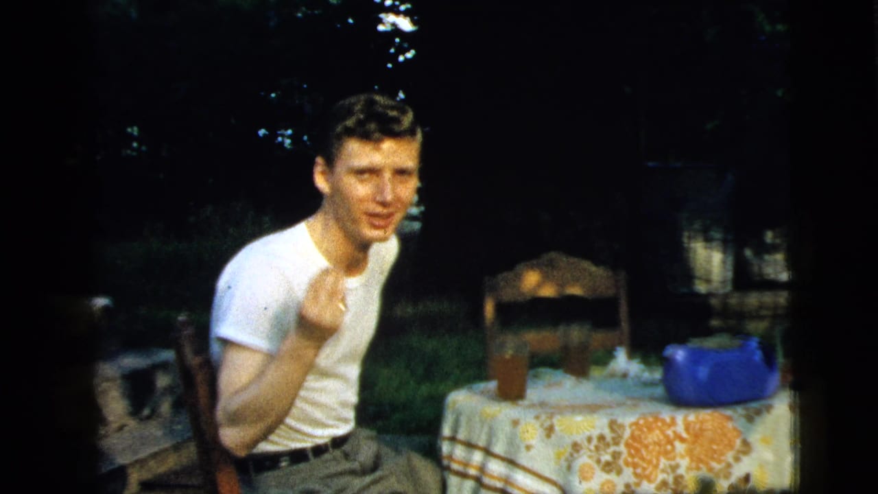 In 1961 Camden, New Jersey home-movie footage, a young man sits at an outdoor table with a floral cloth and blue teapot.