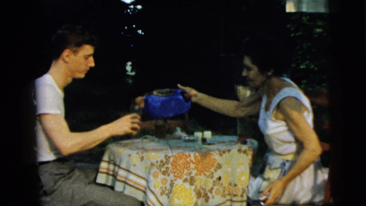 Young man and woman sit at an outdoor table as she reaches toward a blue teapot.