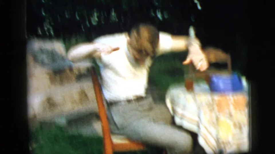 Motion blur captures the young man leaning back beside the floral-covered table in the 1961 Camden backyard scene.