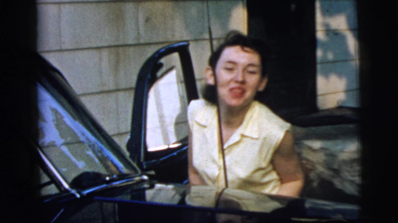 In Camden, New Jersey home-movie footage, a young woman in a pale yellow sleeveless shirt smiles beside the open door of a dark car.
