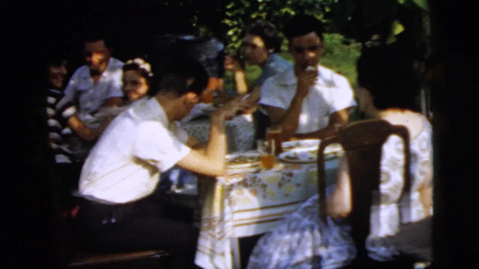 Adults at an outdoor meal in Camden, New Jersey, with a man leaning over the table and others seated behind him.