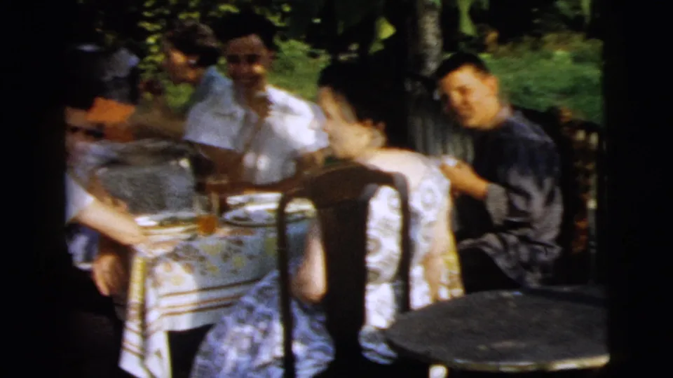 Soft 8mm frame of adults seated around a patterned outdoor table during a 1961 Camden gathering.