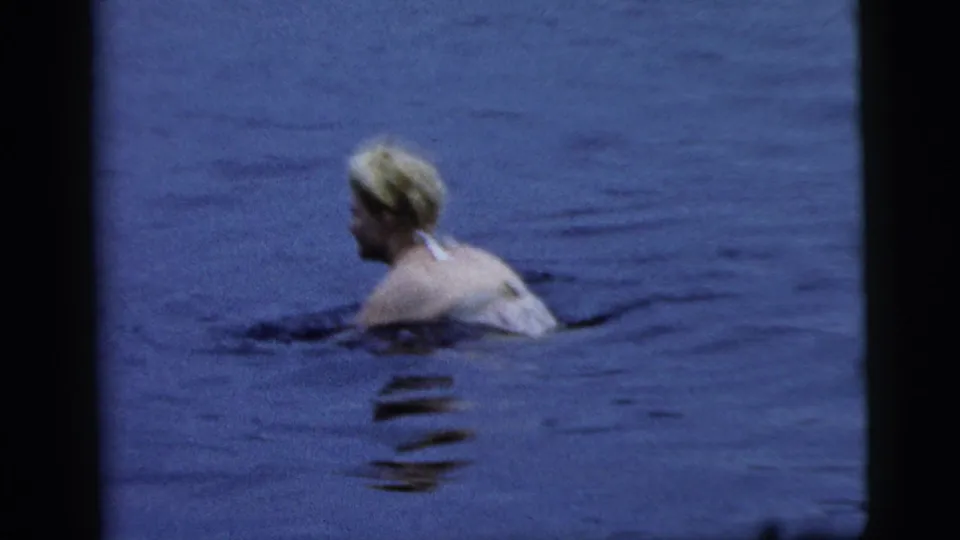 Adult woman swims low in blue-tinted water, with soft 8mm grain and dark frame borders visible.
